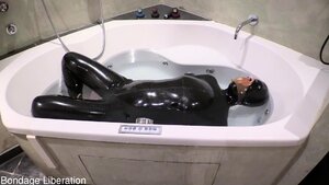 Latex gimp is submersed in the bathtub by a dominatrix